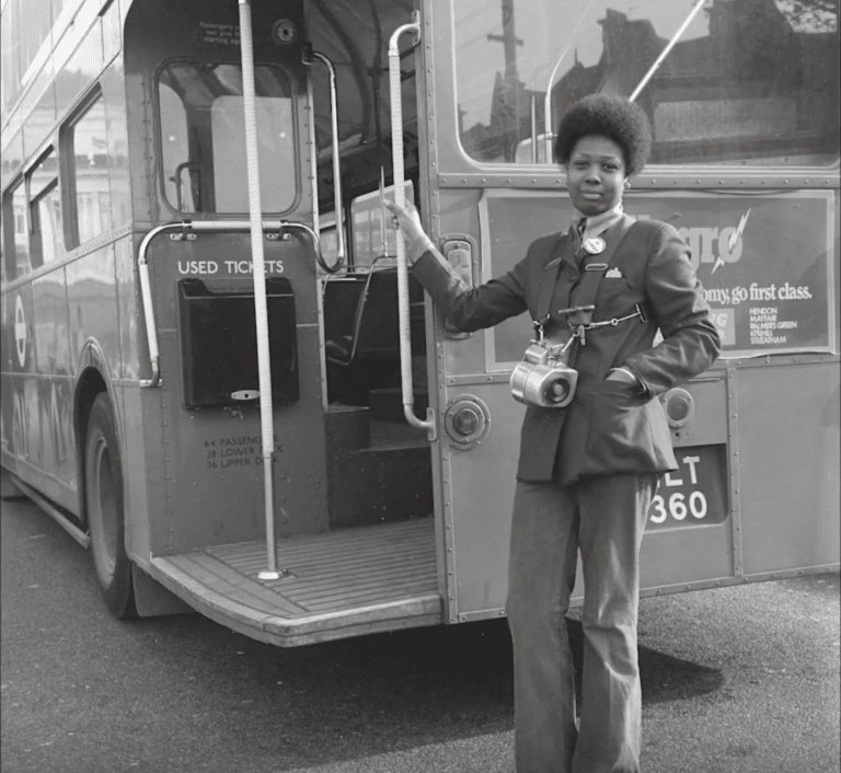 Black and white photograph of a black female ticket conductor next to a vintage double decker bus for the Museum of London 'Last Chance to See' exhibit