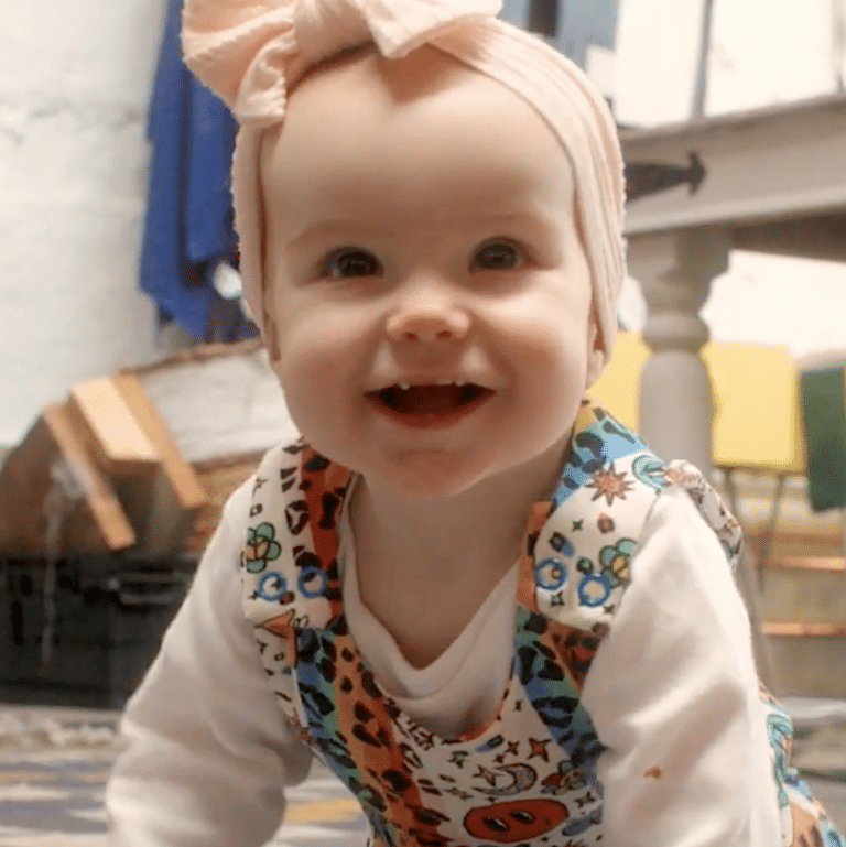 Baby wearing pink head scarf crawls on floor