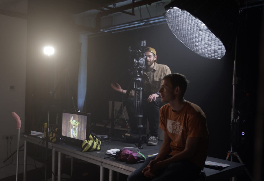 Camera operator shoots in dark room with puppet on monitor